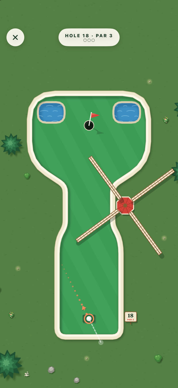 Greens hole 18 from above: a red windmill turning across the fairway, with aiming dots leading up from the ball